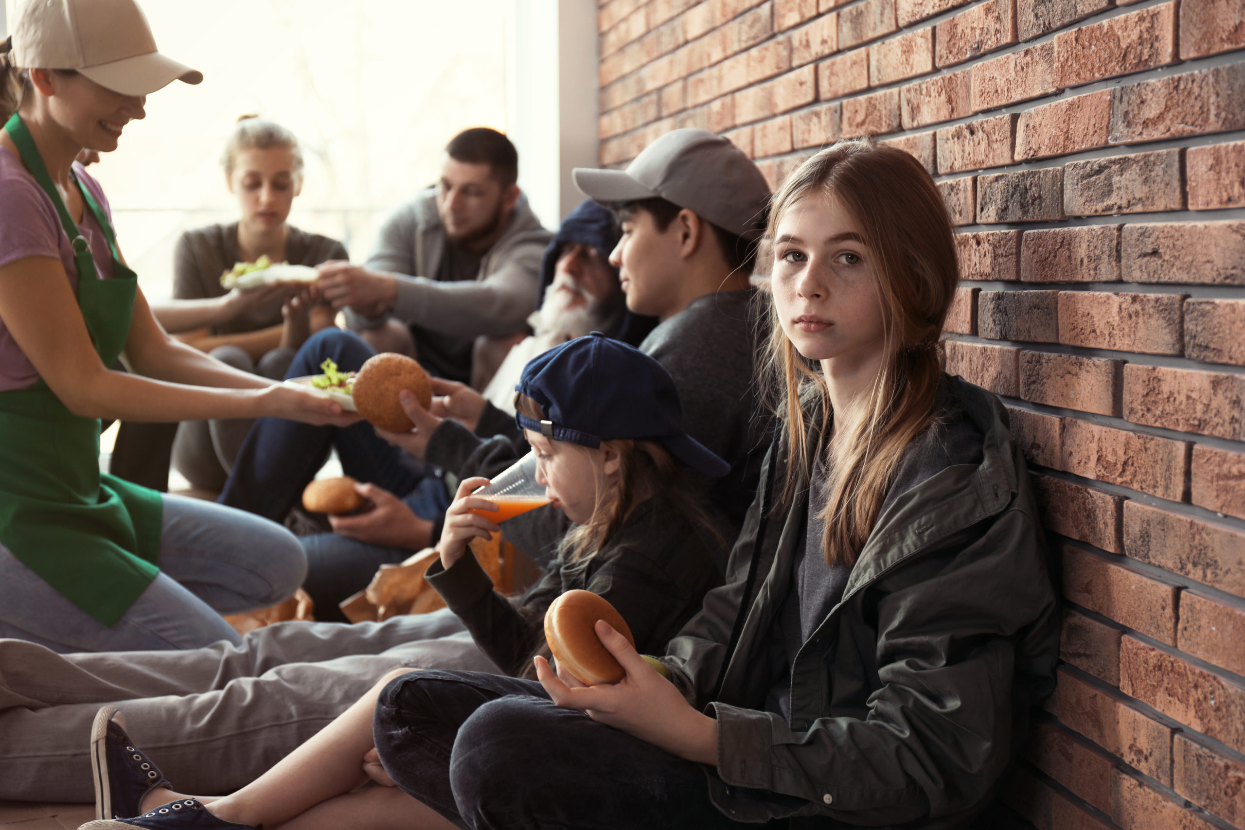 Teenage girl with other people receiving food from volunteers indoors